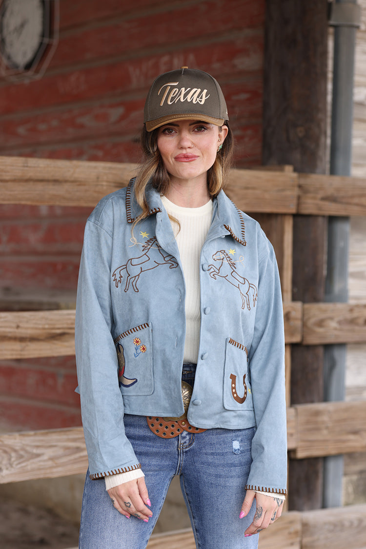 Woman wearing a light blue suede embroidered  jacket with patches, jeans, and a  Texas Embroidered Trucker Hat - Gold/Olive-FleaStyle