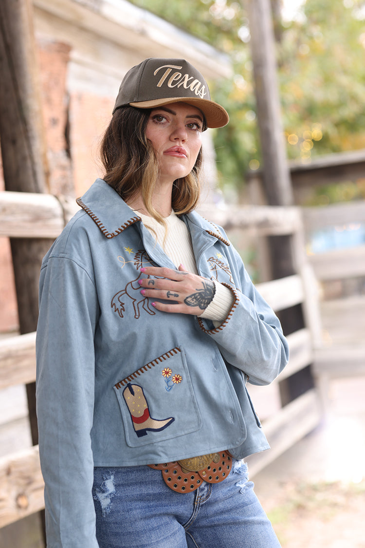 Woman wearing a light blue suede embroidered  jacket with patches, jeans, and a  Texas Embroidered Trucker Hat - Gold/Olive-FleaStyle