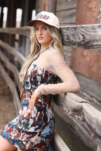 Woman wearing a patterned dress and cap leaning against wooden beams.