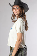 A woman wearing a Roger-Cowboy-Straw-Hat-Black, a cream-colored short-sleeve crop star top, and camouflage pants-FleaStyle